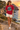 Female model wearing the cardinal-red tee beside a Mediterranean cove