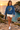 Female model wearing the indigo-blue sweatshirt beside a Mediterranean cove