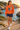 Female model wearing the orange sweatshirt beside a Mediterranean cove