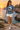 Female model wearing the steel-blue tee beside a Mediterranean cove