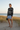 Full-length female model wearing the black botanical all-over-print sweatshirt with tailored pale blue shorts among coastal dunes
