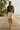 Full-length female model wearing the black botanical all-over-print sweatshirt with tailored cream Bermuda shorts on a beach boardwalk