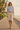 Full-length female model wearing the pastel all-over-print recycled hoodie with tailored cream Bermuda shorts on a beach boardwalk