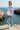 Full-length female model wearing the pastel all-over-print recycled hoodie at a Mediterranean cove