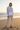 Full-length female model wearing the pastel all-over-print recycled hoodie on a golden-hour beach