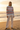 Full-length female model wearing the pastel striped all-over-print sweatshirt with ivory linen pants on a beach