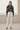 Full-length female model wearing the botanical all-over-print sweatshirt with tailored ivory linen trousers beside the ocean