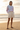 Full-length female model wearing the pastel all-over-print recycled hoodie with tailored ivory shorts on a beach