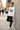 Male model leaning on a concrete wall on a city street in the white ODDSON hooded long-sleeve tee with black chinos