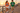 Two models wearing orange and turf-green skeleton-wave tees on a seaside pier