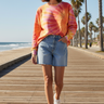 Female model styling the sunburst sweatshirt with denim shorts