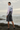 Full-length female model wearing the pastel all-over-print recycled hoodie with tailored charcoal shorts on a Pacific shoreline