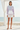 Full-length female model wearing the pastel all-over-print recycled hoodie with tailored white shorts beside the ocean