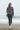 Full-length female model wearing the botanical all-over-print sweatshirt with matte black leggings on a Pacific shoreline