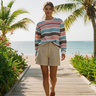 Full-length female model wearing the pastel striped all-over-print sweatshirt with tailored sand shorts on a beach boardwalk