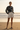 Full-length female model wearing the black botanical all-over-print sweatshirt with tailored ivory shorts on a beach