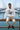 Male model seated on a marina railing in the white ODDSON hooded long-sleeve tee with beige chinos