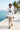 Male model walking a Mediterranean coastal promenade in the white ODDSON hooded long-sleeve tee with linen trousers